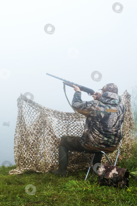 Скачать Охотник на водоплавающую птицу стреляет в летящую утку. фотосток Ozero