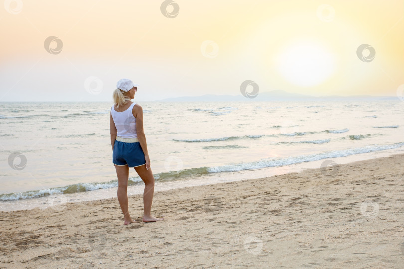 Скачать женщина стоит и наблюдает за солнцем на пляже на закате. фотосток Ozero