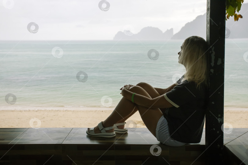 Скачать Портрет молчаливой женщины, сидящей на террасе и размышляющей, на фоне моря, дождливого. фотосток Ozero