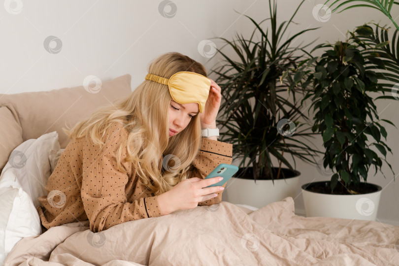 Скачать Женщина в постели с телефоном, задумчивое выражение лица. фотосток Ozero