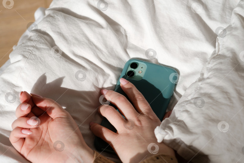 Скачать Рука, держащая смартфон на кровати фотосток Ozero