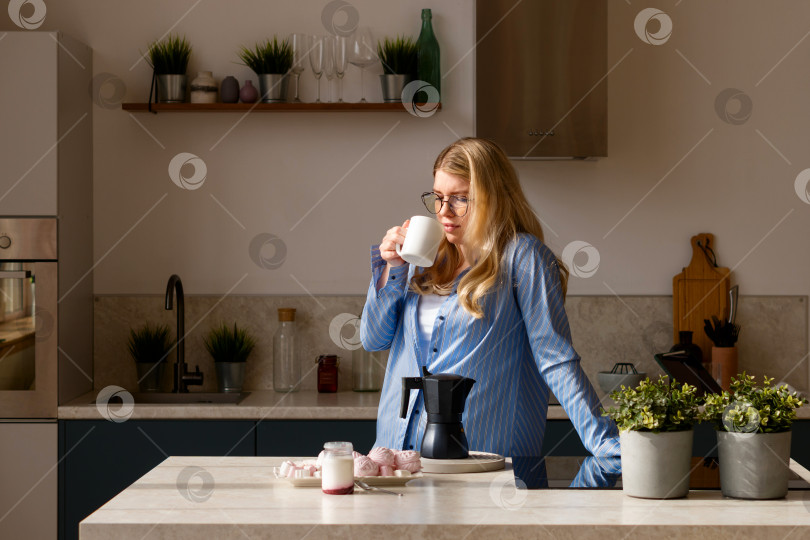 Скачать Женщина пьет кофе на залитой солнечным светом кухне фотосток Ozero