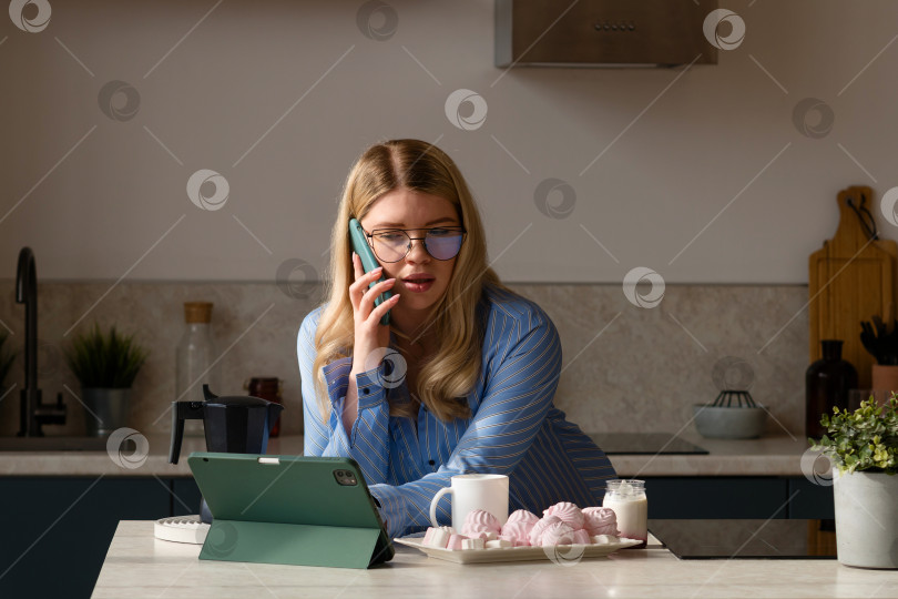 Скачать Женщина разговаривает по телефону с завтраком на кухне фотосток Ozero