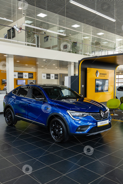 Скачать Синий внедорожник Renault Arkana в автосалоне. Автомобиль крупным планом. На заднем плане - рабочие места специалистов по обслуживанию и продажам. Автосалон Renault в Мега Адыгея. фотосток Ozero