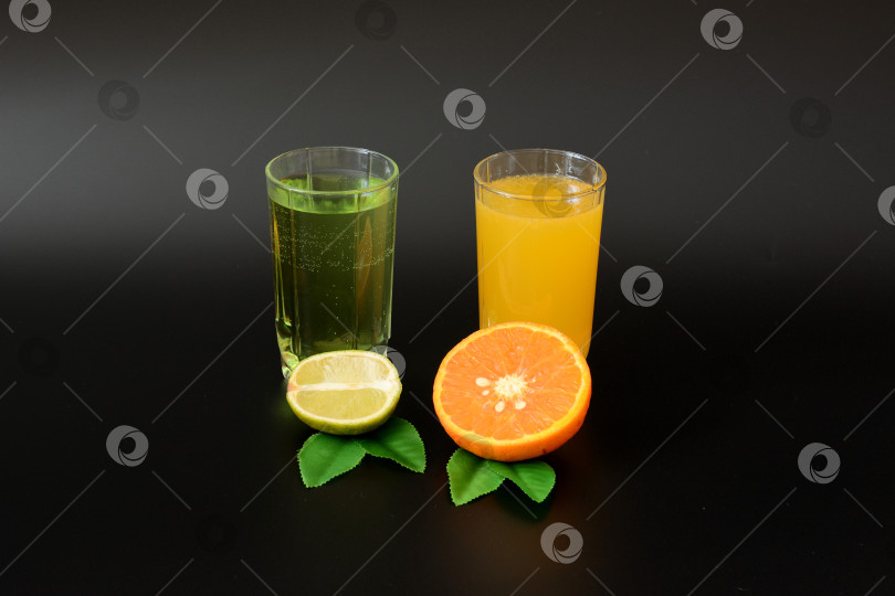 Скачать Два бокала с цитрусовыми соками на черном фоне, рядом половинка спелого лайма и апельсин с листьями. фотосток Ozero