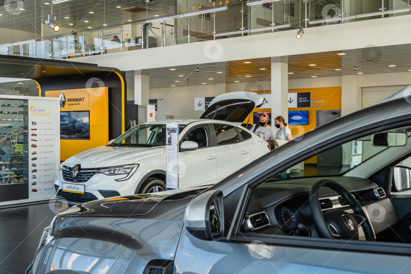 Скачать Белый внедорожник Renault Arkana в автосалоне. Парень и девушка в защитных черных масках осматривают багажное отделение автомобиля. Крупный план. Автосалон Renault в Мега Адыгея. Краснодар, Россия - 17 августа 2021 г. фотосток Ozero