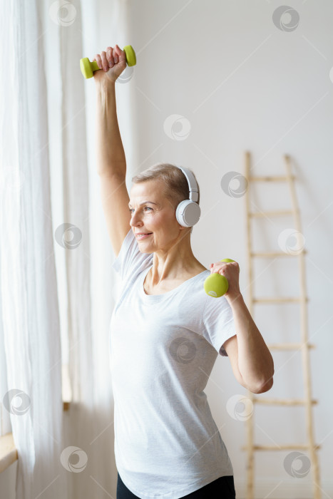 Скачать Портрет счастливой пожилой женщины, выполняющей фитнес-упражнения с гантелями дома фотосток Ozero