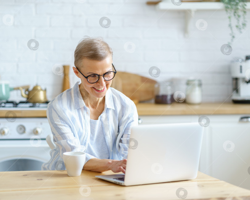 Скачать Счастливая женщина средних лет печатает что-то на клавиатуре во время работы или учебы на ноутбуке дома фотосток Ozero