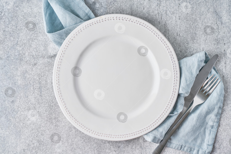 Скачать Пустая чистая белая круглая тарелка на фоне серой льняной скатерти со столовым серебром фотосток Ozero