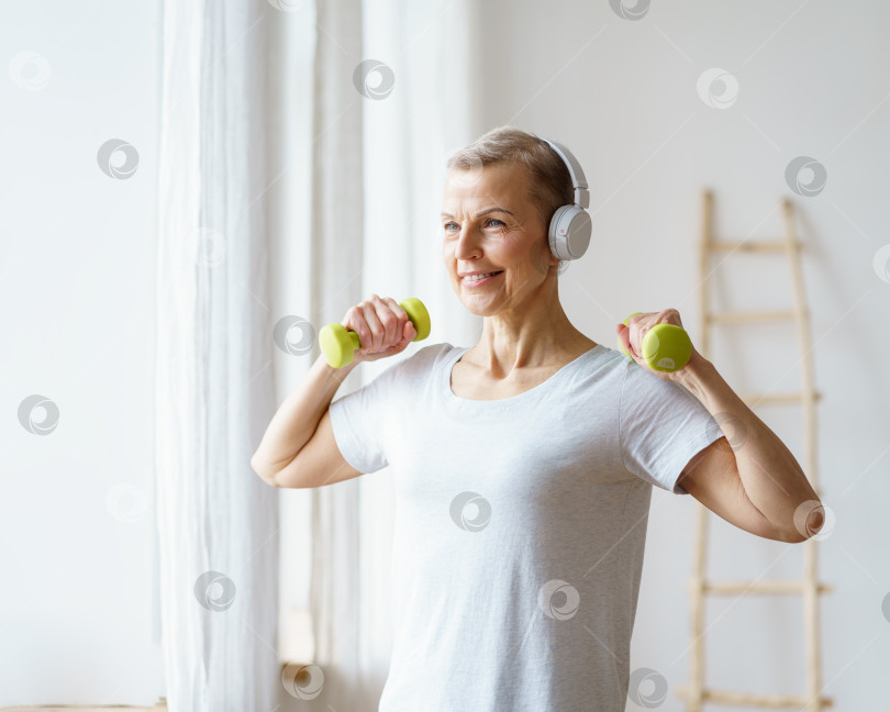 Скачать Портрет счастливой пожилой женщины, выполняющей фитнес-упражнения с гантелями дома. Зрелая женщина фотосток Ozero