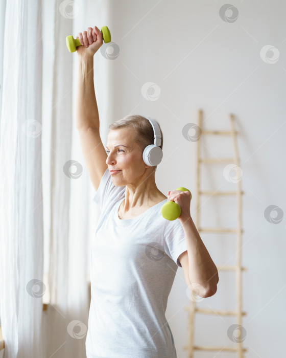 Скачать Портрет счастливой пожилой женщины, выполняющей фитнес-упражнения с гантелями дома. Зрелая женщина, вертикаль фотосток Ozero