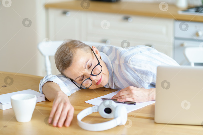Скачать Зрелая женщина спит на столе на кухне у себя дома, делая перерыв во время работы или учебы онлайн фотосток Ozero