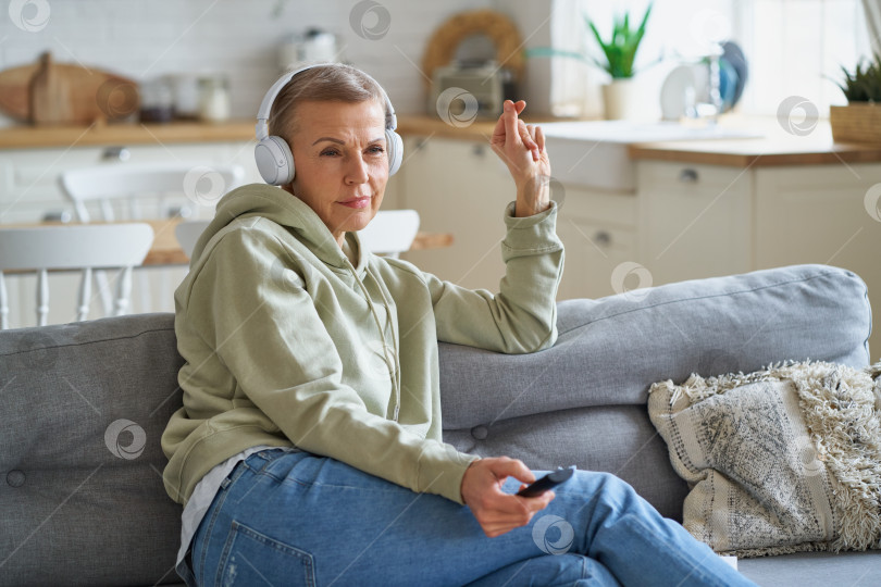 Скачать Счастливая женщина средних лет смотрит телевизор, сидя дома на диване фотосток Ozero
