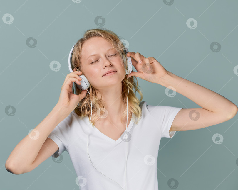 Скачать Крупным планом портрет молодой женщины с закрытыми глазами, слушающей музыку через наушники в нейтральном сером тоне фотосток Ozero