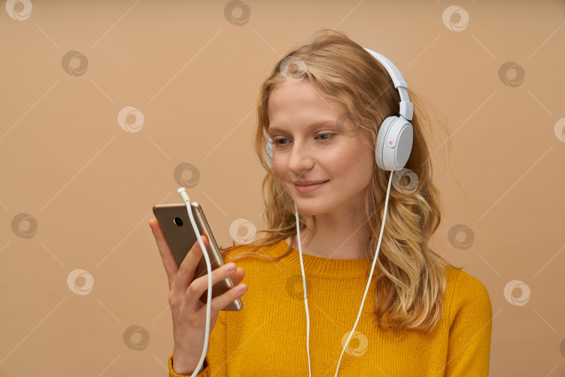 Скачать Крупным планом портрет молодой женщины, слушающей музыку в наушниках на стене желто-бежевого оттенка фотосток Ozero