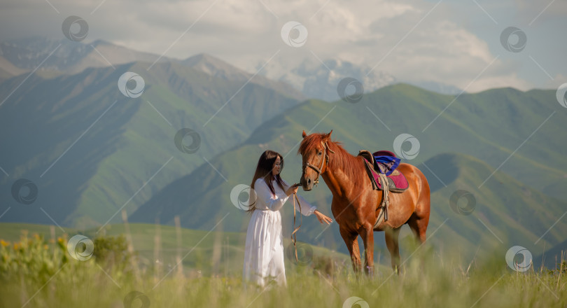 Скачать Азиатская девушка (киргизка) в белом платье прогуливается с лошадью на природе на фоне гор, Бишкек, Кыргызстан фотосток Ozero