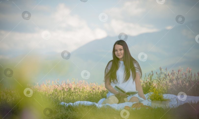 Скачать Девушка 20-25 лет, весной и летом, сидит в поле на природе на пикнике в шляпке и в белом платье, ест фрукты и читает книгу фотосток Ozero