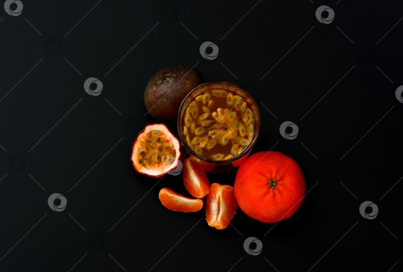Скачать Стакан фруктового сока с косточками на черном фоне, рядом с кусочками спелого мандарина-маракуйи. фотосток Ozero