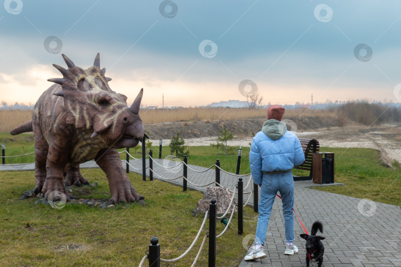 Скачать Девушка с собакой около фигуры стиракозавра в Динопарке Янтарного фотосток Ozero