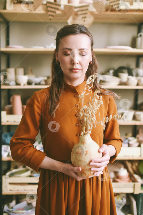 Скачать Творческая женщина-гончар с глиняной вазой в мастерской ремесленника с закрытыми глазами фотосток Ozero