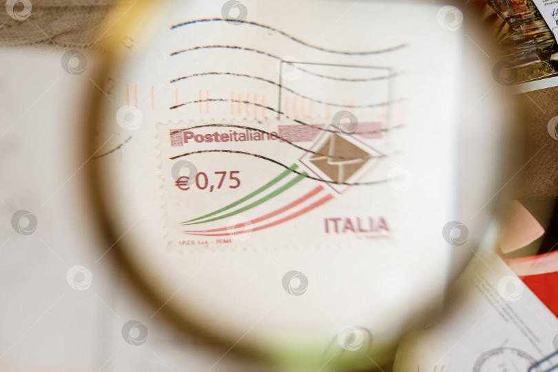 Скачать 10 января 2022 года Москва, Россия - почтовая марка Poste italiane на почтовой открытке с увеличительным стеклом фотосток Ozero