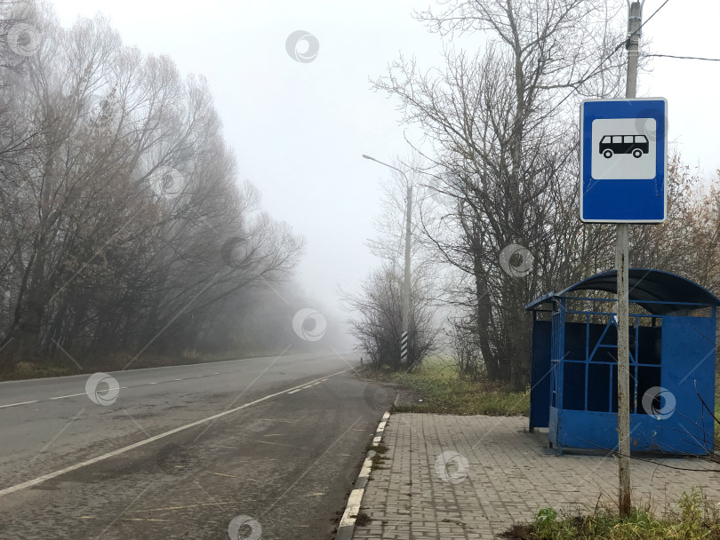 Скачать Пустая автобусная остановка на обочине асфальтированной дороги туманным осенним утром фотосток Ozero