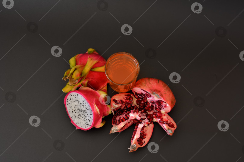 Скачать Бокал со смесью тропических фруктов на черном фоне, рядом с ним - разломанный плод граната с косточками и спелый срез питайи. фотосток Ozero