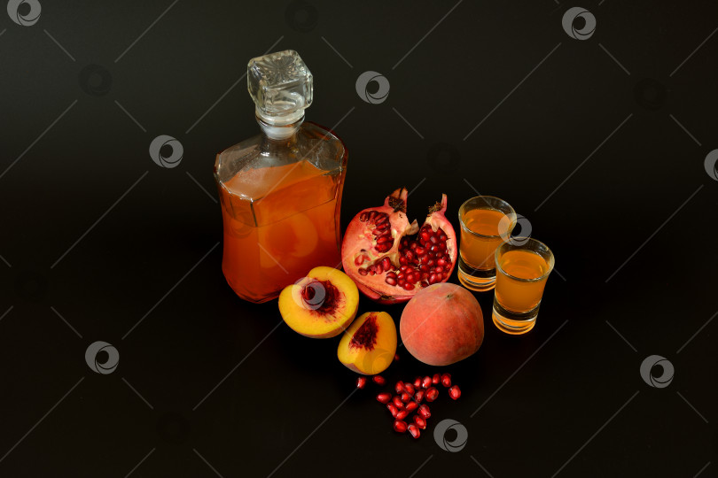 Скачать Гранатово-персиковый ликер, домашний алкоголь в двух бокалах и бутылке на черном фоне, рядом спелые фрукты. фотосток Ozero