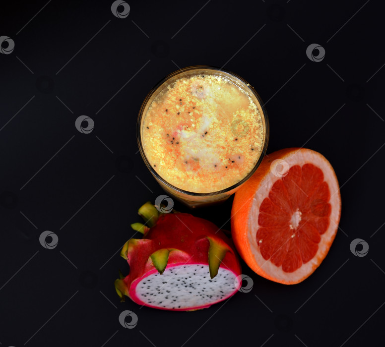 Скачать Высокий стакан свежевыжатого сока из тропических фруктов на черном фоне, рядом с половинкой спелой питайи и грейпфрутом. фотосток Ozero