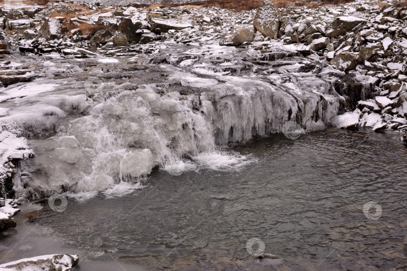 Скачать Небольшая горная речка замерзшим каскадом стекает в долину со скалистыми хребтами, припорошенными первым снегом. фотосток Ozero