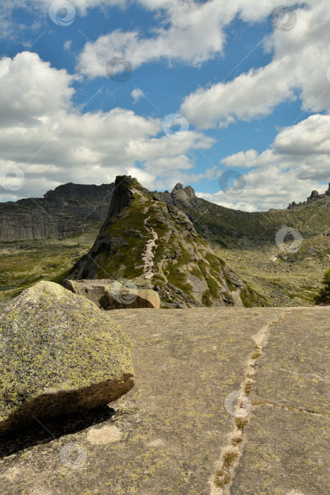 Скачать Глядя поверх больших скал на узкую пешеходную тропу, которая проходит вдоль вершины остроконечной горы в пасмурный летний день. фотосток Ozero