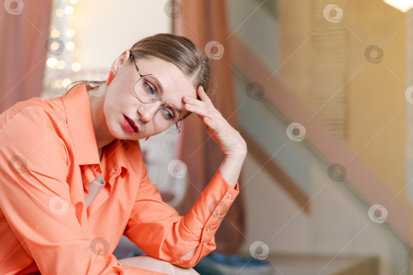 Скачать Женщина в оранжевой рубашке сидит на стуле и смотрит вниз фотосток Ozero