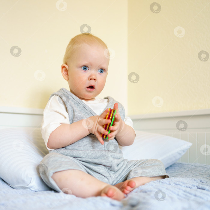 Скачать Маленький мальчик играет с магнитной строительной игрушкой, сидя на кровати фотосток Ozero