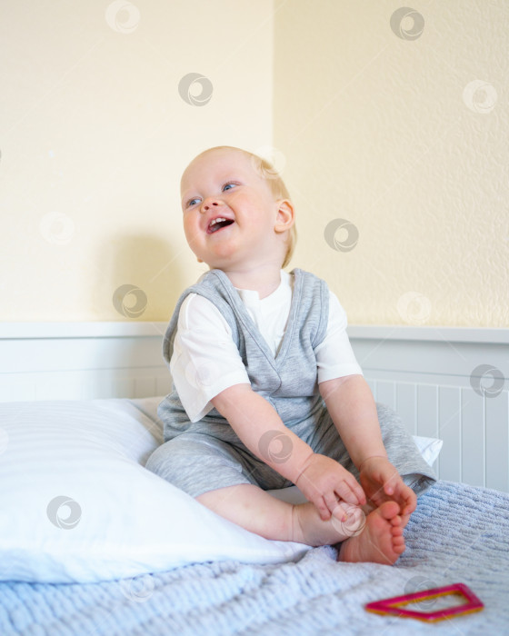 Скачать Милый маленький мальчик наслаждается игрой с магнитной строительной игрушкой, сидя на кровати фотосток Ozero