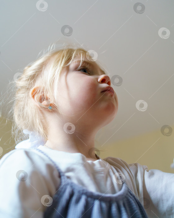 Скачать Красивая маленькая девочка смотрит на что-то, играя в помещении фотосток Ozero