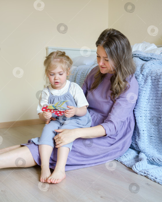 Скачать Молодая улыбающаяся мама проводит время с маленькой дочкой в детской комнате фотосток Ozero