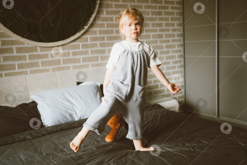 Скачать Очаровательная расслабленная маленькая девочка играет с плюшевым мишкой на большой кровати у себя дома фотосток Ozero