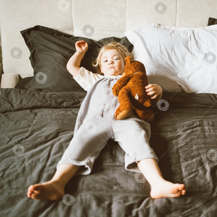 Скачать Очаровательная расслабленная маленькая девочка играет с плюшевым мишкой на большой кровати у себя дома фотосток Ozero
