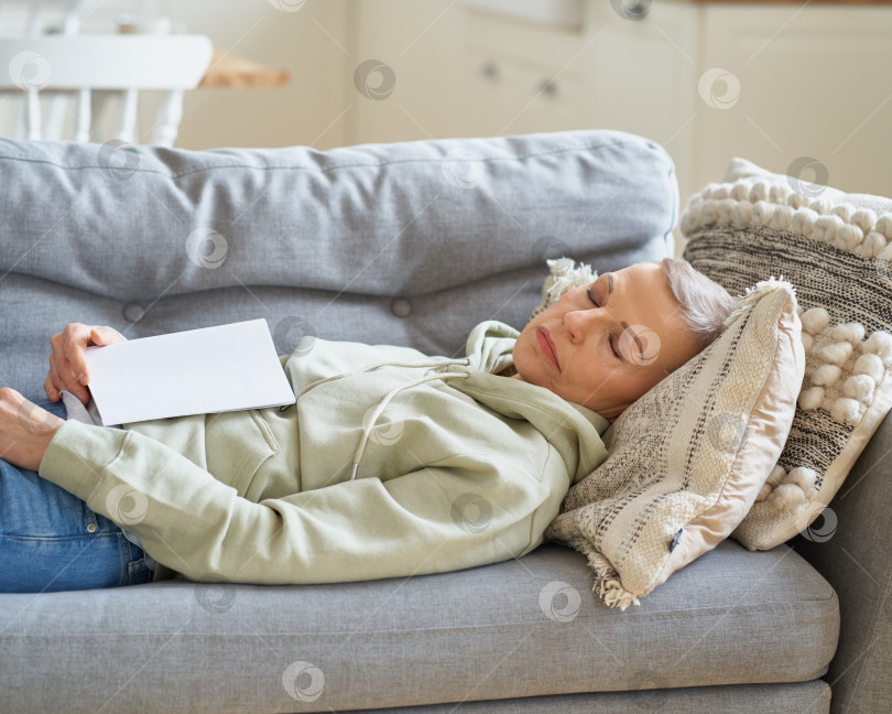 Скачать Пожилая женщина, прикорнувшая на диване, заснула дома после чтения книги фотосток Ozero