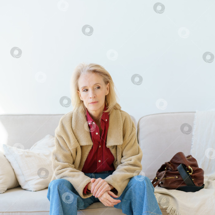 Скачать Усталая пожилая женщина смотрит в сторону, отдыхая дома на диване после тяжелого рабочего дня фотосток Ozero
