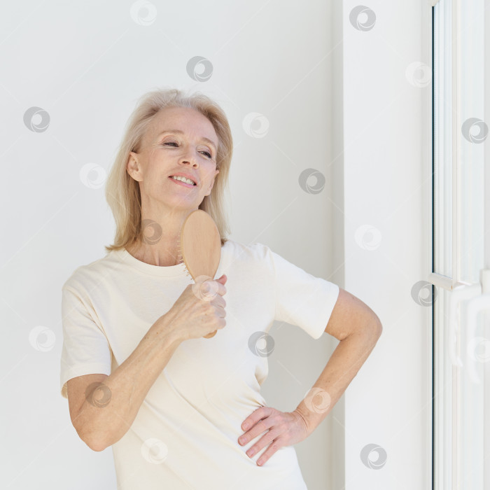 Скачать Счастливая пенсионерка веселится дома, напевая расческой свою любимую песню и глядя в окно фотосток Ozero