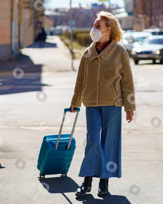Скачать Пожилая женщина лет 60 с синим чемоданом путешествует одна во время эпидемии коронавируса фотосток Ozero