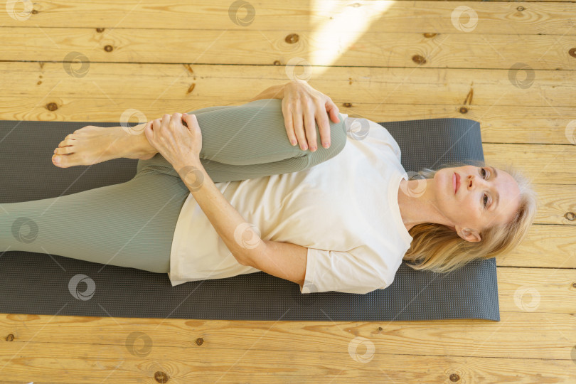 Скачать Активная пенсионерка, делающая упражнения на растяжку по утрам на коврике для йоги у себя дома фотосток Ozero