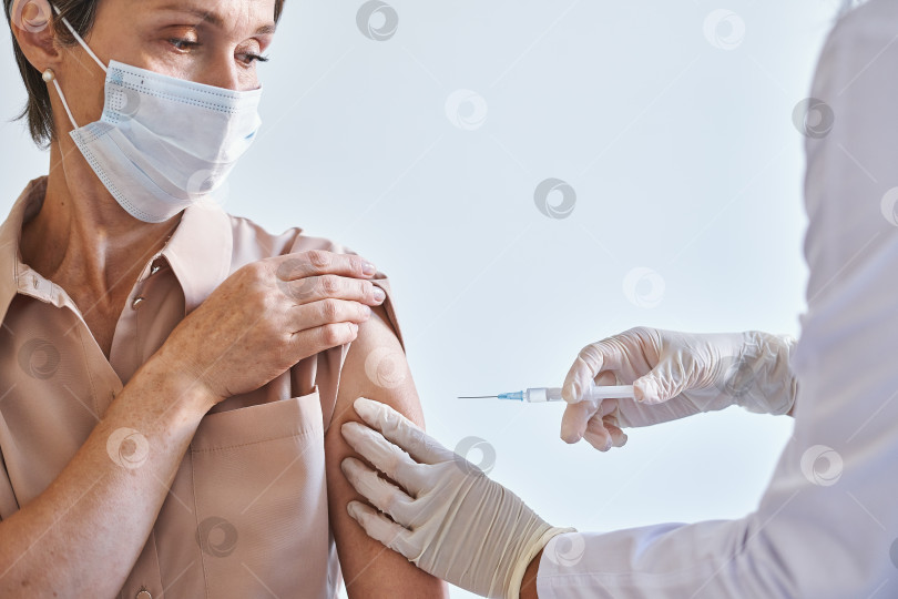 Скачать Женщина средних лет в медицинской маске на лице получает инъекцию вакцины против коронавируса covid19 фотосток Ozero