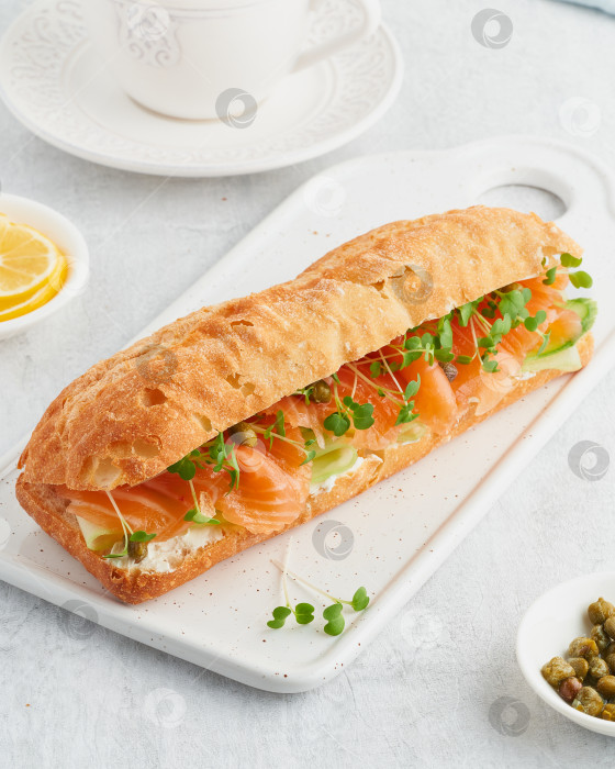 Скачать Большой сэндвич с лососем, сливочным сыром и ломтиками огурца на белом бетонном столе. фотосток Ozero