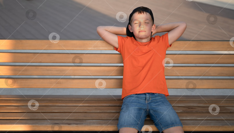 Скачать Симпатичный мальчик сидит на скамейке и мечтает, отдыхает. фотосток Ozero