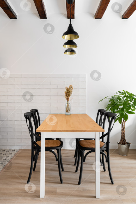 Скачать Деревянный обеденный стол с вертикальной рамой и четырьмя дизайнерскими стульями с лампами и деревянными балками на фоне белой кирпичной стены и растений. Современная кухня в новой квартире. Copyspace фотосток Ozero