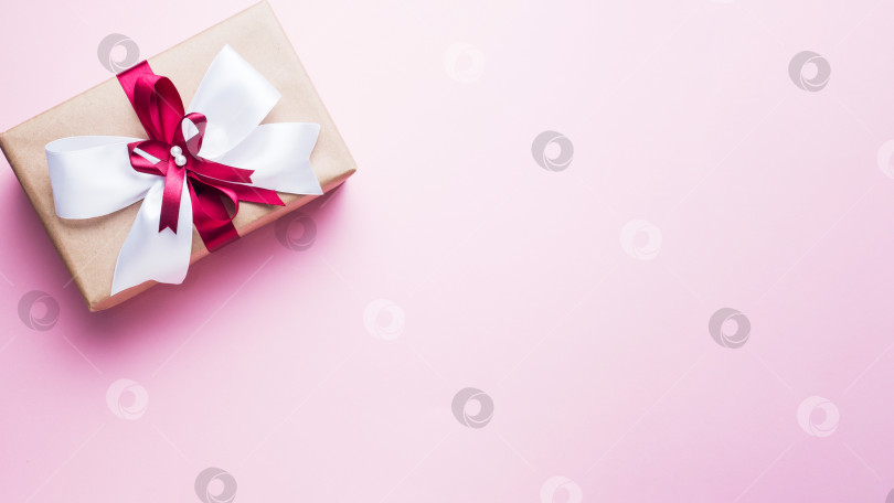 Скачать Подарочная коробка с большим бантом на розовой столешнице. Композиция из флэтлея на Рождество, день рождения, день матери или свадьбу. фотосток Ozero