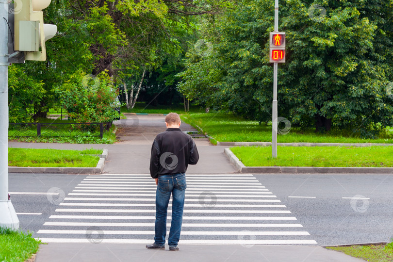 Скачать Мужчина на пешеходном переходе ждет зеленого сигнала светофора, чтобы перейти дорогу фотосток Ozero