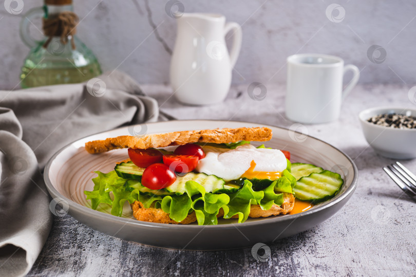 Скачать Бутерброд из вафельного хлеба с яйцом-пашот и овощами на тарелке на столе фотосток Ozero